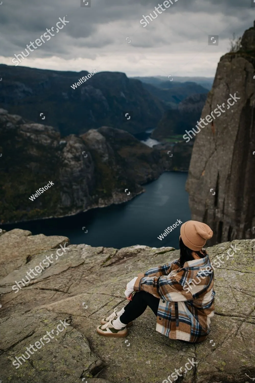 A woman sitting on a cliff above a deep blue fjord
