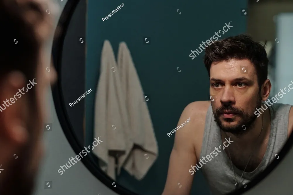 A man looking at his reflection in a bathroom mirror
